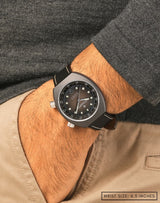 Man wearing Earthshine wristwatch, hand in pocket, showing its pale-brown fume dial and sleek matte Cerasteel™ case.