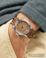 Man wearing Cover Drive Pitch wristwatch with hand in pocket, featuring the matte-brown dial and polished stainless steel case.